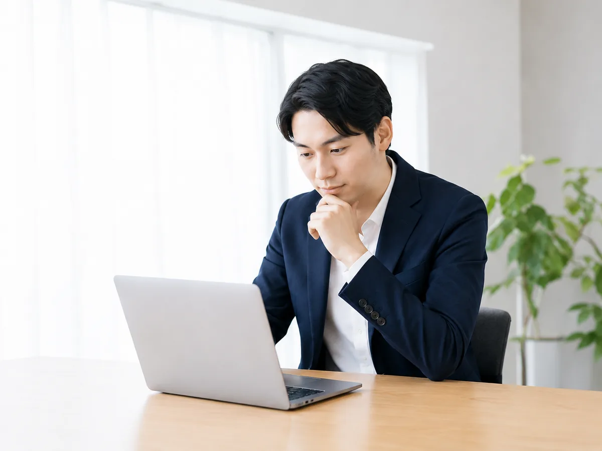 ノートパソコンを見ながら考える男性